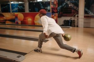 A man practicing rolling a bowling ball down the alley.