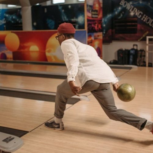 A man practicing rolling a bowling ball down the alley.
