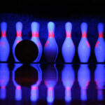 Bowling pin about to be hit by a bowling bowl, glowing under the black light of the bowling alley.